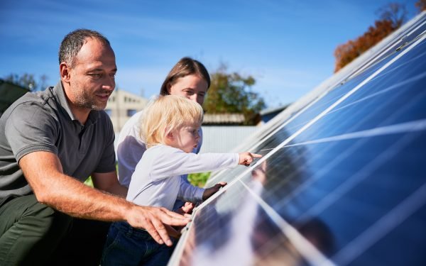 Mann, kvinne og et lite barn studerer et solcellepanel som gir Enovastøtte.